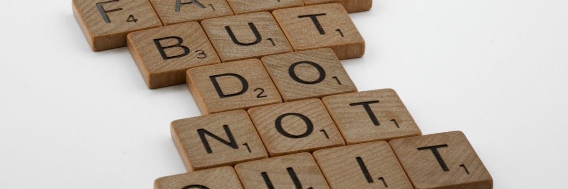 Close-up of Scrabble tiles forming the motivational phrase 'Fail but do not quit' on a white surface.